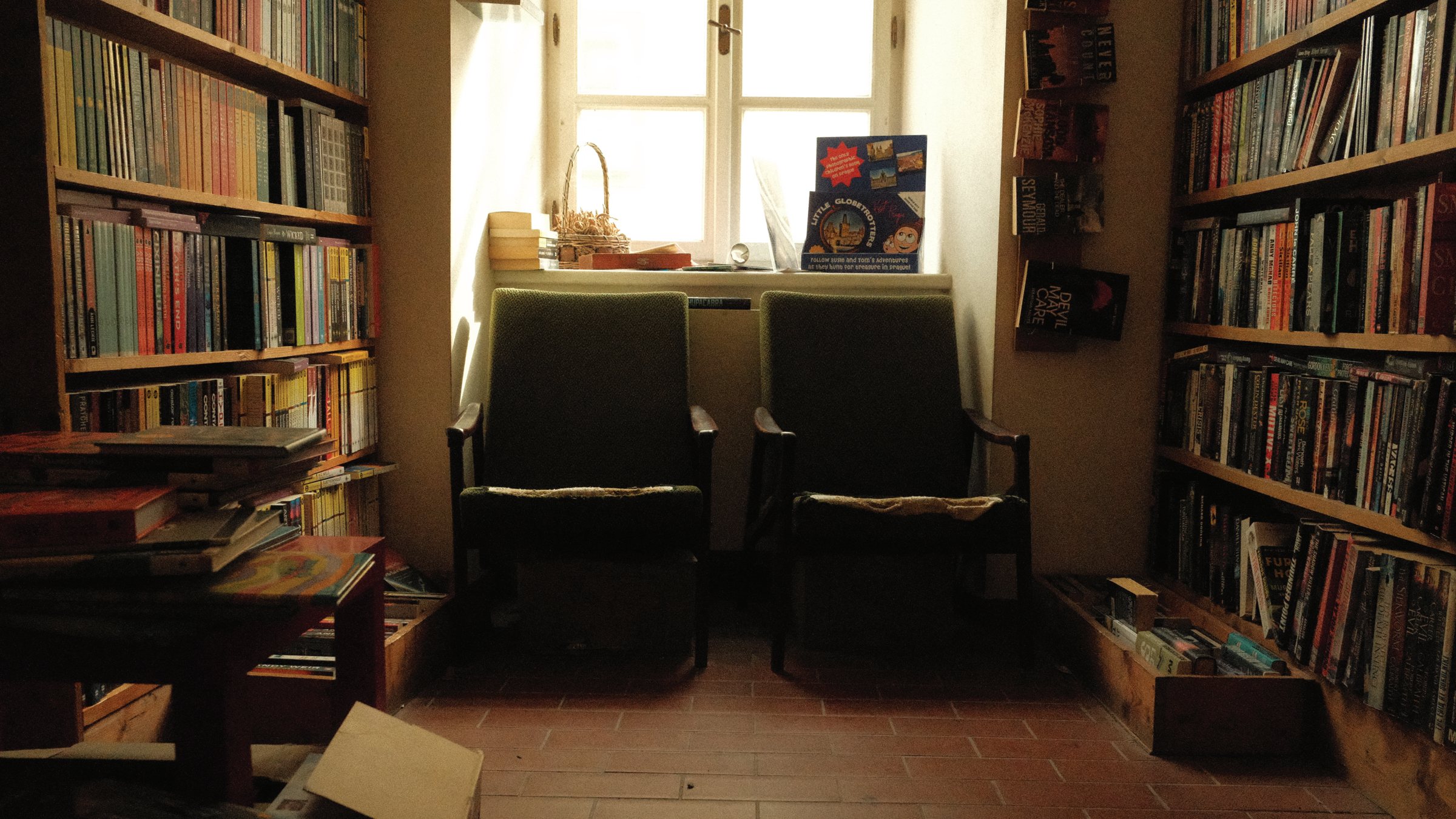 Quiet bookshop corner with two green armchairs beneath a window