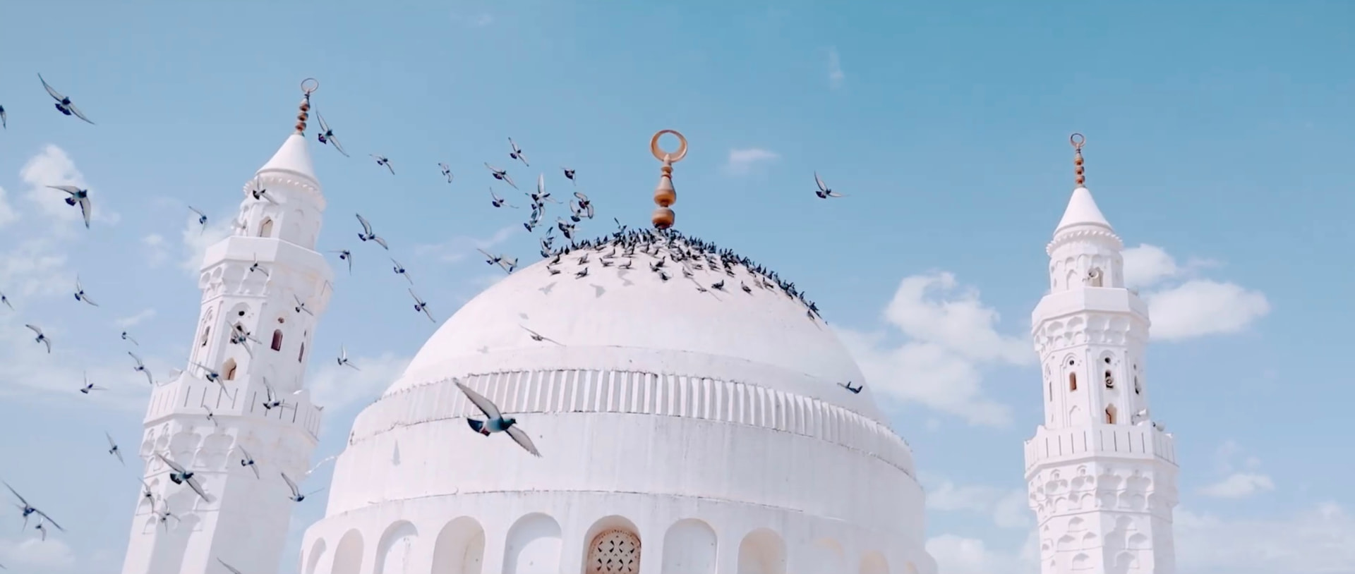 White mosque dome and minarets with doves flying against a blue sky — على خطى الرسول
